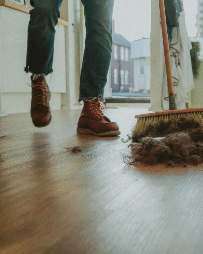 Man wearing boots and jeans sweeping floor of barbershop